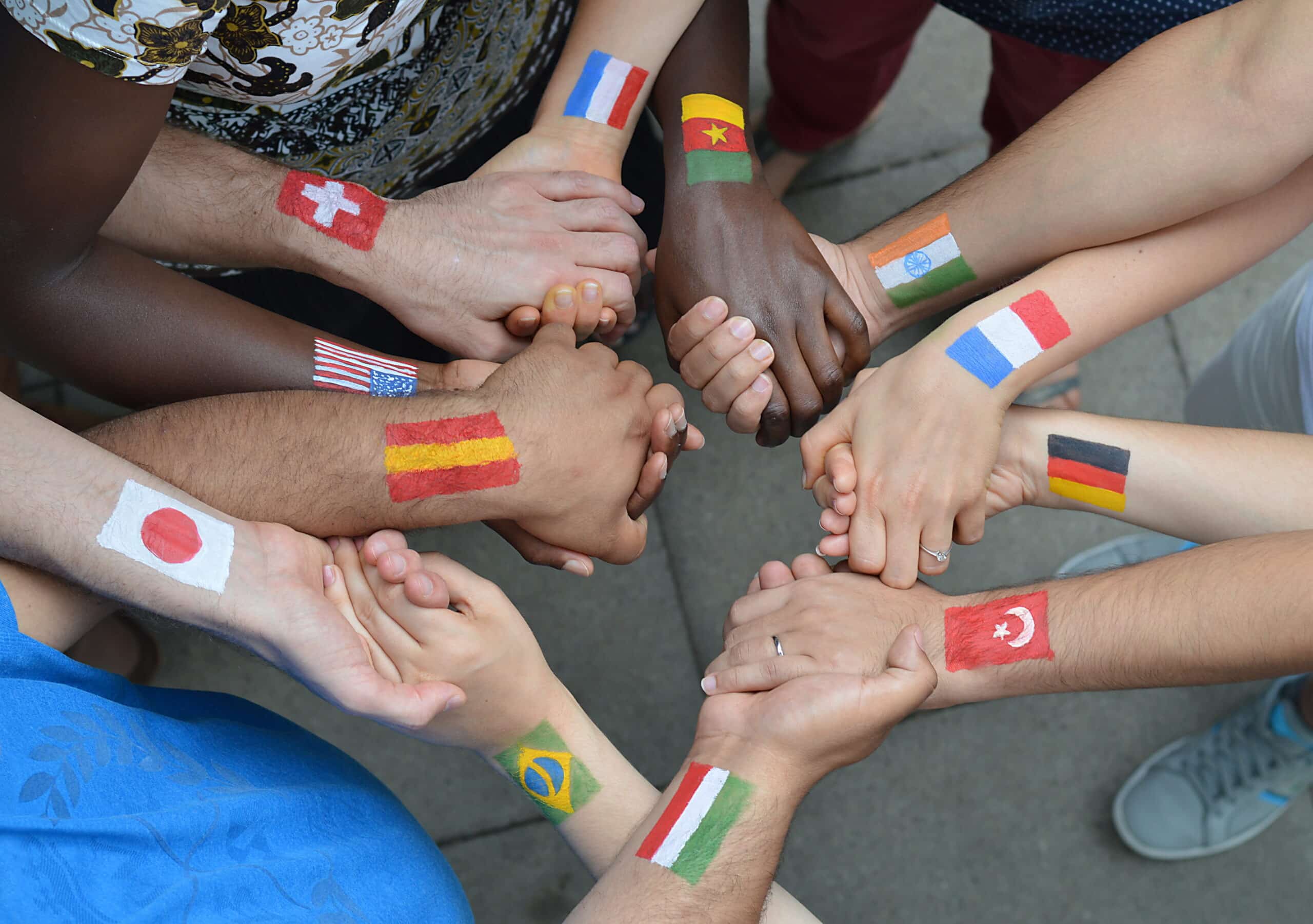 Internationale Brüder und Schwestern mit unterschiedlichen Flaggen auf ihren Armen gemalt stehen miteinander im Kreis und halten sich die Hände.